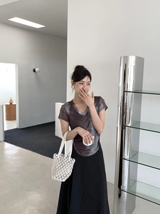 Detail of a white woven bucket bag paired with a grey tie-dye T-shirt and black maxi skirt