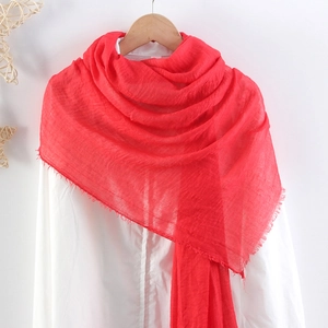 Detail of red crinkled linen scarf with frayed edges hanging on a white wooden hanger