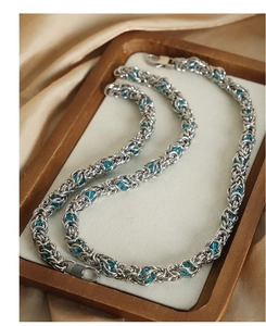 Detail of silver titanium curb chain necklace with blue beads on a silk background