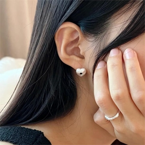 Close-up of textured silver heart studs and minimalist ring worn by a model