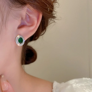 Close-up of green oval emerald earrings with double-layered cubic zirconia halo on ear