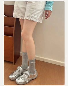 Detail von grauen Netzsocken im Ballett-Stil mit weißer Schleife und silbernen Sneakern