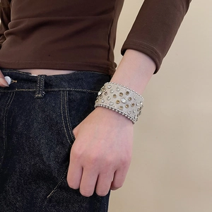 Gros plan sur un large bracelet en cuir beige orné de strass brillants et de rivets