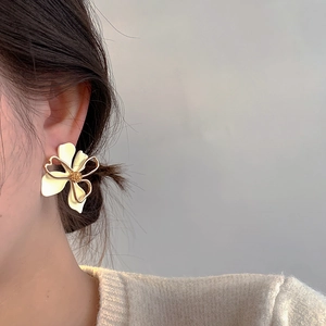 Close-up of elegant hollow-out cream floral earrings with gold trim on model ear