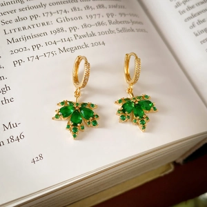Macro detail of gold-plated maple leaf earrings with green zircon on a vintage book