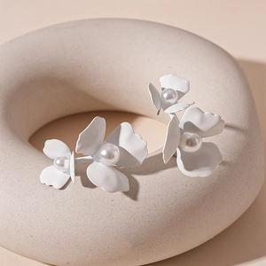 Detail of white matte flower stud earrings with a pearl center on a minimalist display