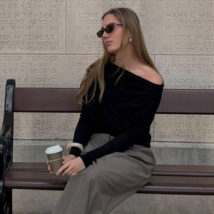 Chic black one-shoulder long sleeve top and grey pants on a woman sitting outdoors