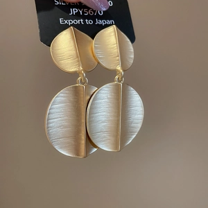 Detail of matte gold brushed round pendant earrings with unique leaf shape design