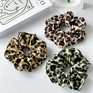 Three-piece leopard print satin scrunchie set in assorted colors on a textured surface