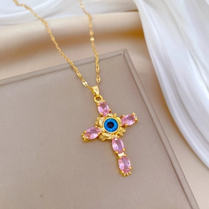 Gold cross necklace with blue evil eye and pink crystals on beige jewelry box