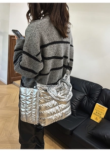 Silver quilted metallic puffer tote bag with wide strap worn by a model in interior