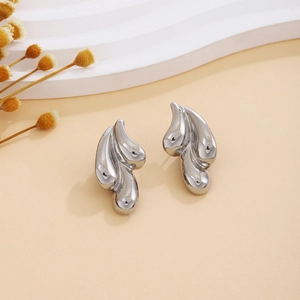 Detailed view of polished silver irregular geometric earrings on a beige background