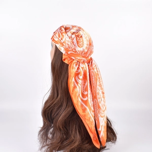 Detail of orange paisley print satin square scarf worn as a headwrap on a mannequin head