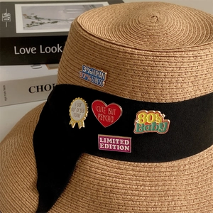 Kreative Emaille-Pins mit Zitaten und Herzformen auf einem Strohhut dekoriert