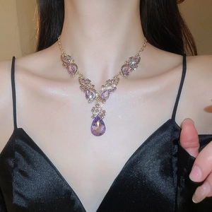 Close-up of a sparkling purple teardrop pendant necklace with diamonds on a model