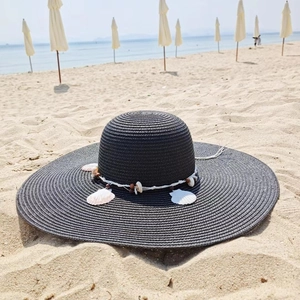 Detail of black straw sun hat with shell and bead band on a sunny tropical beach