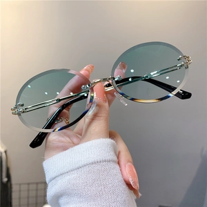 Détail de lunettes de soleil ovales sans monture, verres dégradés verts et branches dorées