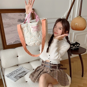 Détail du sac matelassé à fleurs crème avec anses roses et bandoulière en toile orange