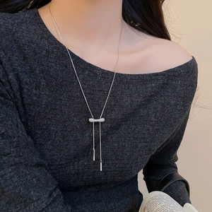 Détail du collier à pampilles argentées avec pendentif en zircone sur un pull sombre