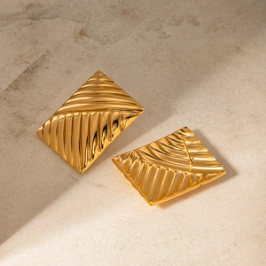 Detail shot of golden rectangular earrings with ribbed texture on beige stone background