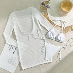 Flat lay of white three-piece bikini set with long sleeve crochet cover-up on sand