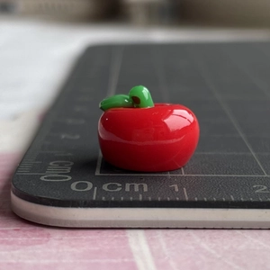 Macro shot showing a 1cm mini resin red apple accessory on a centimeter scale pad