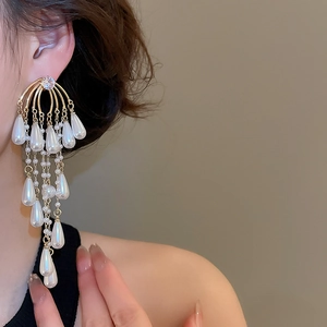 Macro detail of elegant golden fringe earrings with white teardrop pearls and zircons