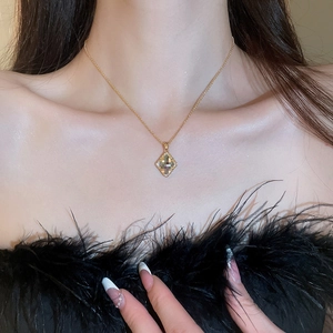 Close-up of gold clover necklace with dark square gemstone worn by model in black top