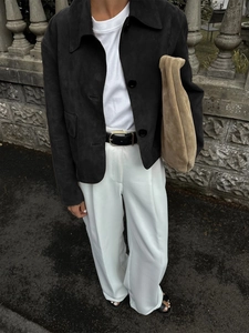 Women's casual black suede button-up jacket paired with white trousers and a clutch bag
