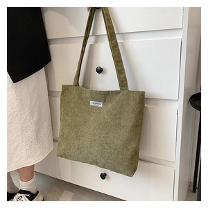 Detail of green corduroy tote bag with Fashion label hanging on a wooden drawer