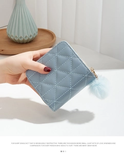 Detail of light blue quilted wallet with gold zipper and decorative pompom keychain