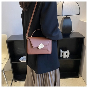 Detail of a brown leather crossbody bag with gold metal buckle on a model in a minimal room