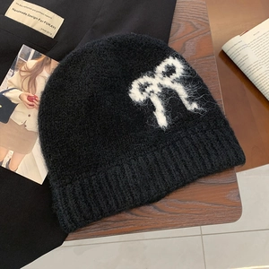 Close-up of black mohair knit beanie featuring a white bow pattern on a wooden surface