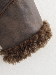 Detailed close-up of brown suede fabric with thick faux fur trim on a winter jacket