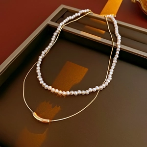 Detail of double-layer necklace with white pearls and gold snake chain on a vintage tray