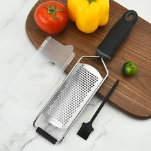 Detail of stainless steel grater with black handle and brush on marble background