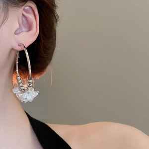 Detailed view of silver hoop earrings featuring white acrylic flowers worn by a model