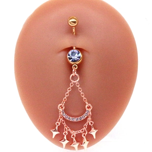 Détail macro d'un piercing de nombril or rose avec gemme bleue et breloques étoiles