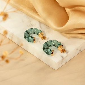 Transparent green resin C-shape twist earrings with gold studs on marble and silk