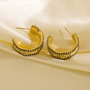Detail of 14K gold-plated C-shape earrings with green zircons and hammered metal texture