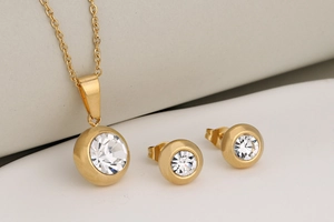 Close-up of gold stainless steel jewelry set with round bezel-set crystals on white surface