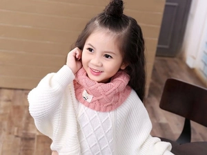 Detail of pink knitted kids' snood featuring a diamond pattern and cute cartoon tag