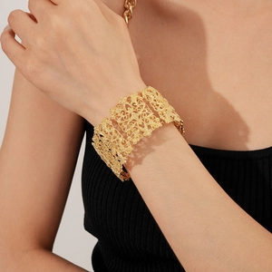Detailed view of wide golden cuff bracelet featuring intricate filigree hollow patterns