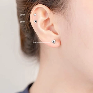 Detailed comparison of 3mm and 5mm silver heart stud earrings on a model's ear