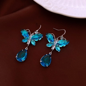 Detailaufnahme der Schmetterlingsohrringe mit blauen Kristallen und Silberhaken auf Stoff