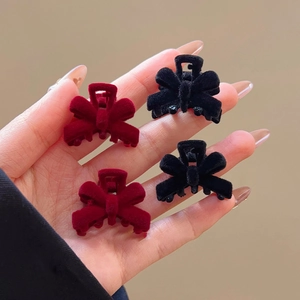 Detail view of small red and black velvet bow hair clips held in hand for hair styling