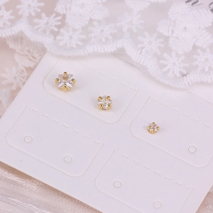 Macro detail of three golden square zircon stud earrings on white lace background