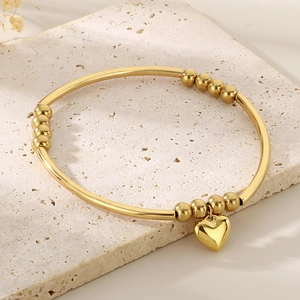 Gros plan du bracelet à pendentif cœur en acier doré avec des perles rondes polies