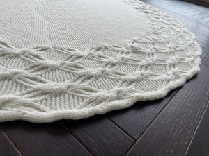 Detail of white knitted Christmas tree skirt featuring intricate scalloped edges and mesh texture