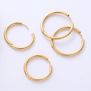 Macro detail of four minimalist gold-plated hoop earrings with hinged closures on white surface